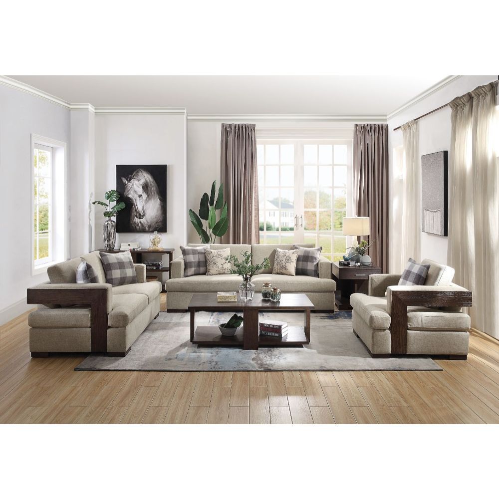 Entire Niamey Living Room collection shown together in a decorated living room. The collection includes an accent chair, a loveseat, a sofa, an end table, an accent table, and a coffee table. The upholstery is light gray with wooden accents that have a rich walnut finish.